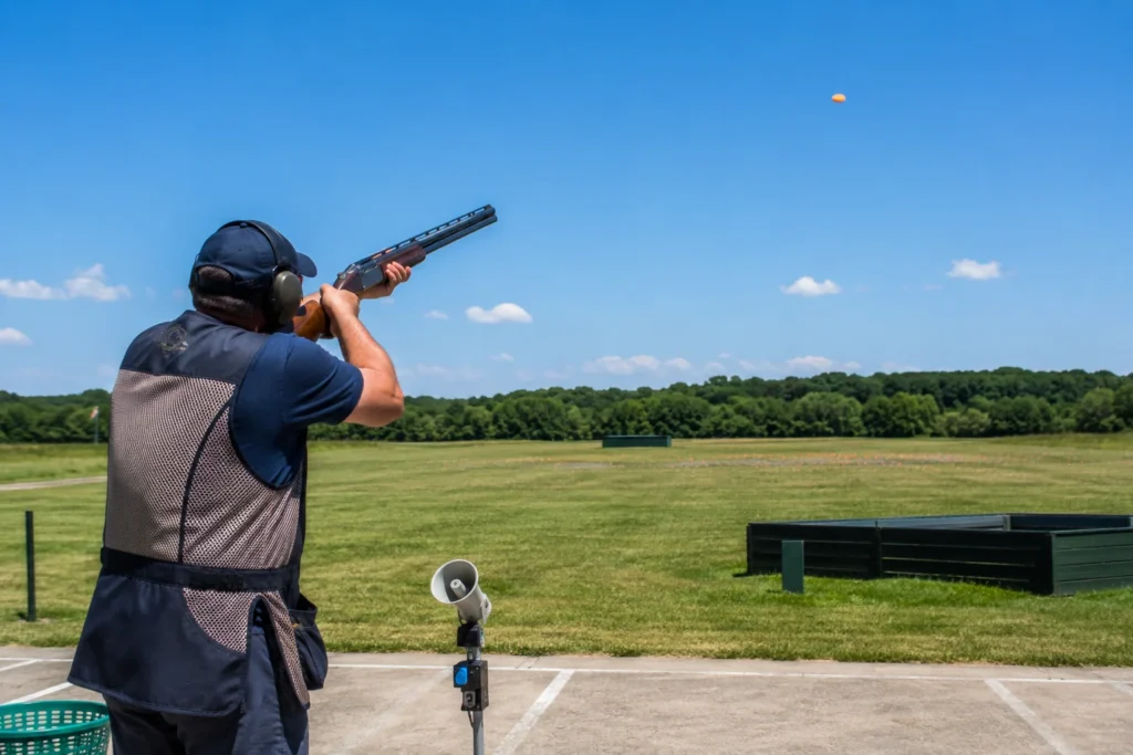 Un tireur de dos sur un pas de tir, arme épaulée, un plateau orange en vol